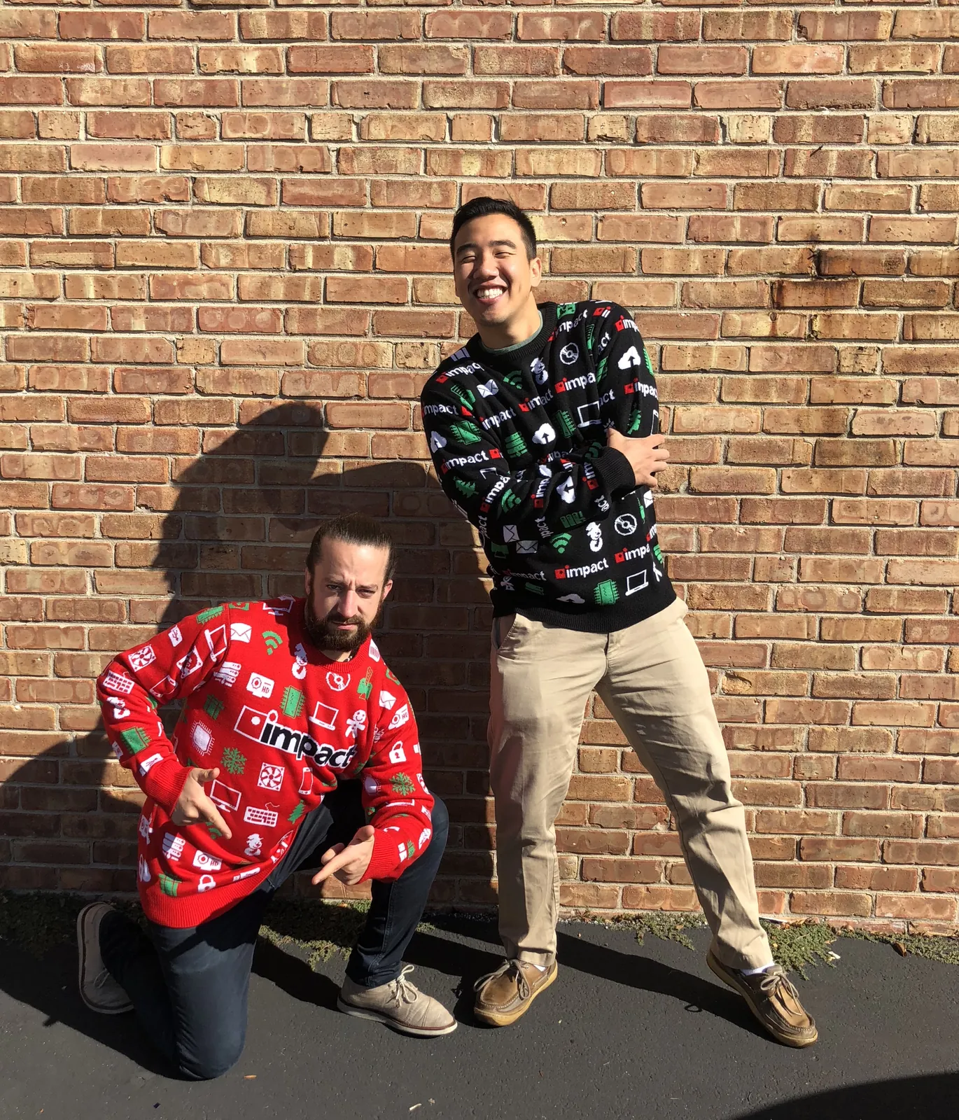 Two people wearing red and black impact branded holiday sweaters