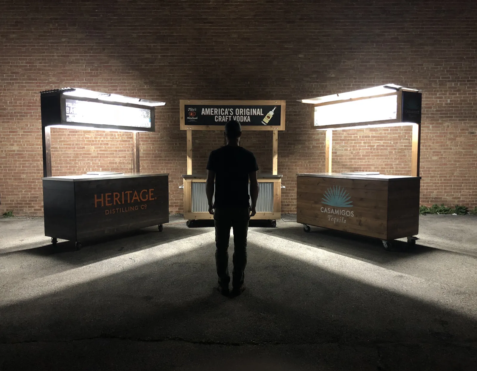 Heritage, Tito’s and Casamigos bar carts illuminated against a brick wall at night