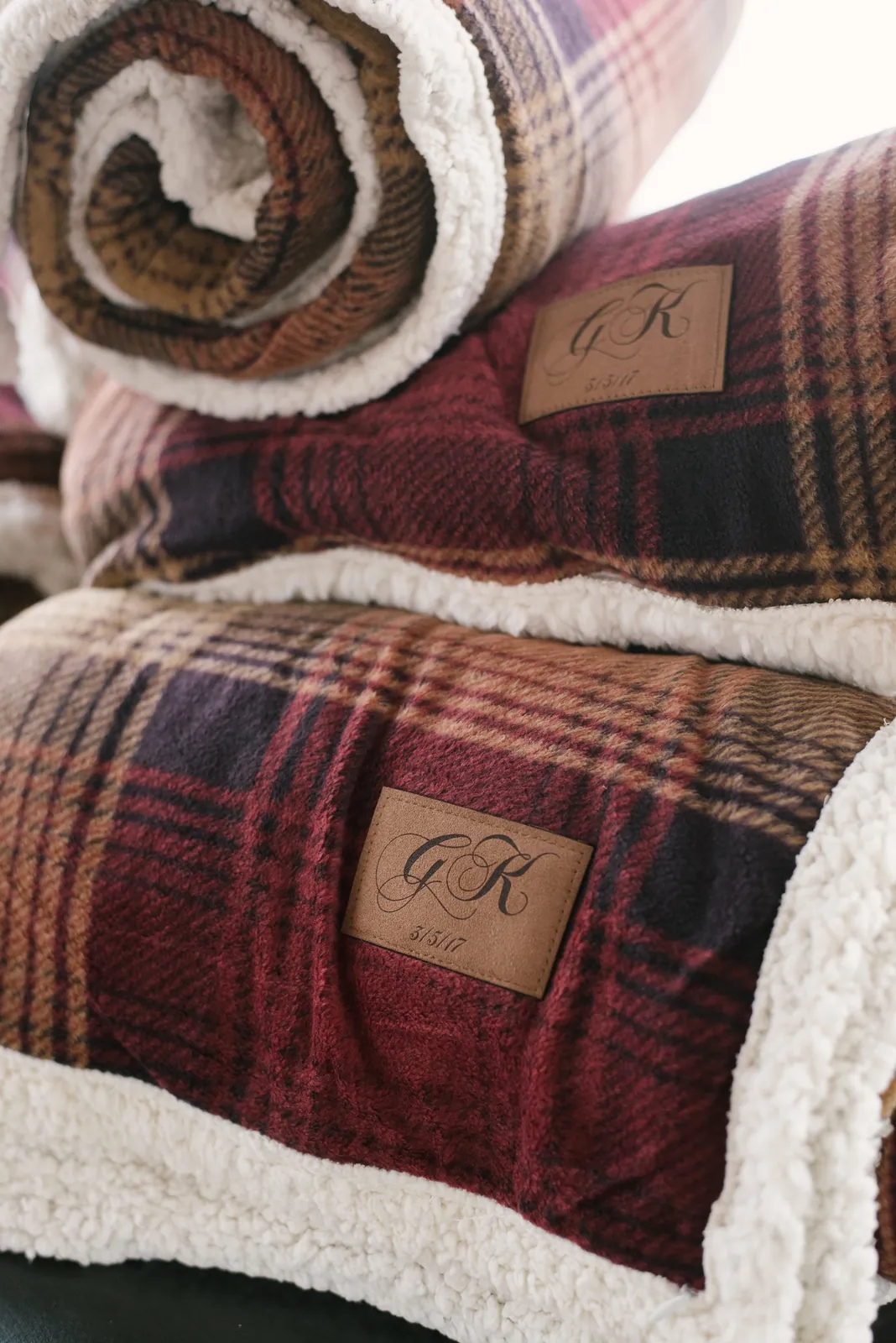 Rolled plaid sherpa blankets finished with monogrammed leather patches