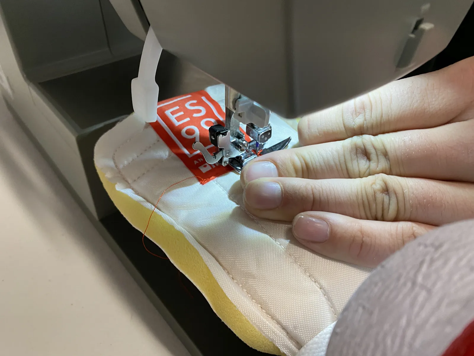 Close-up of hands guiding white fabric with a red label through a sewing machine